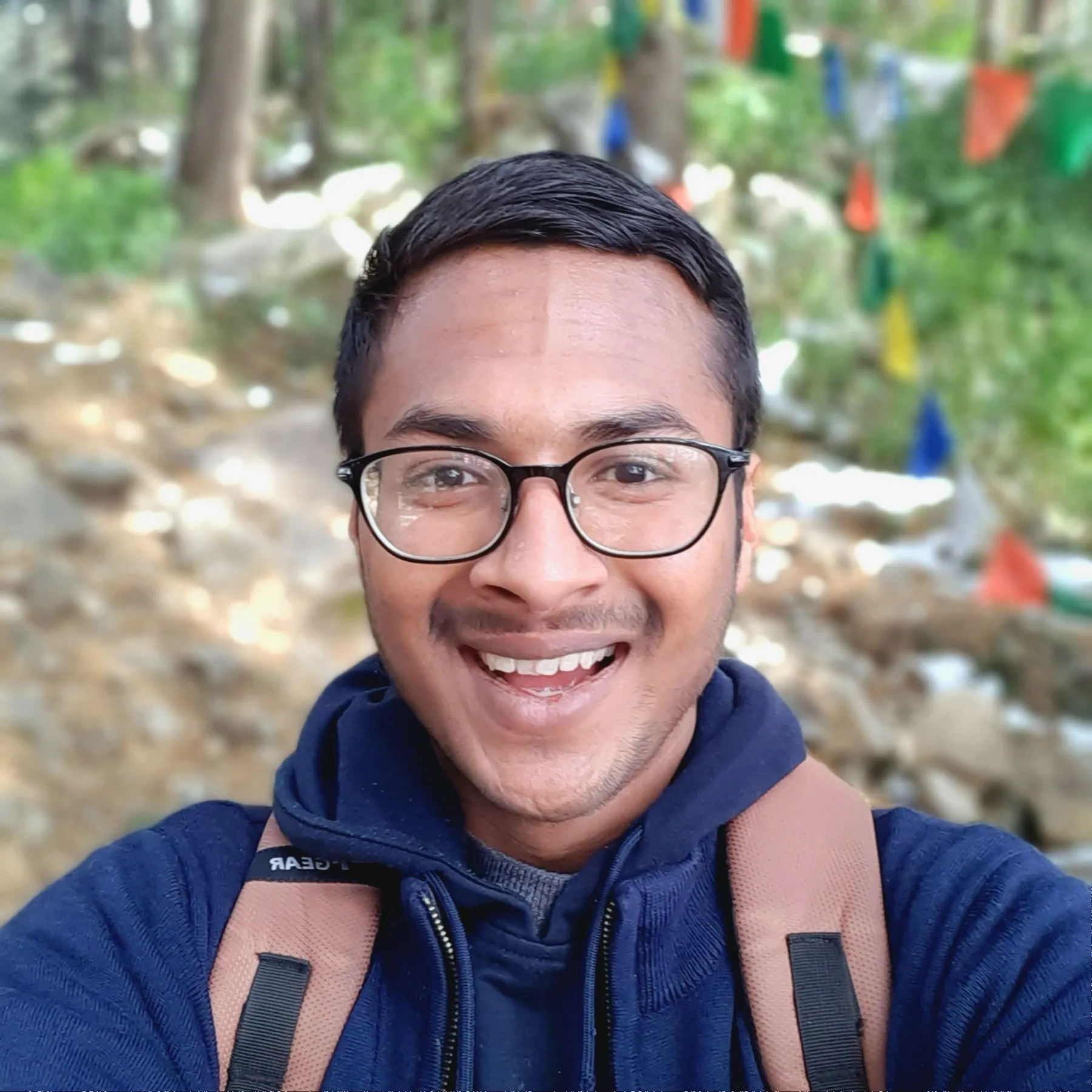 Gantavya grinning on a mountain trail strung with prayer flags